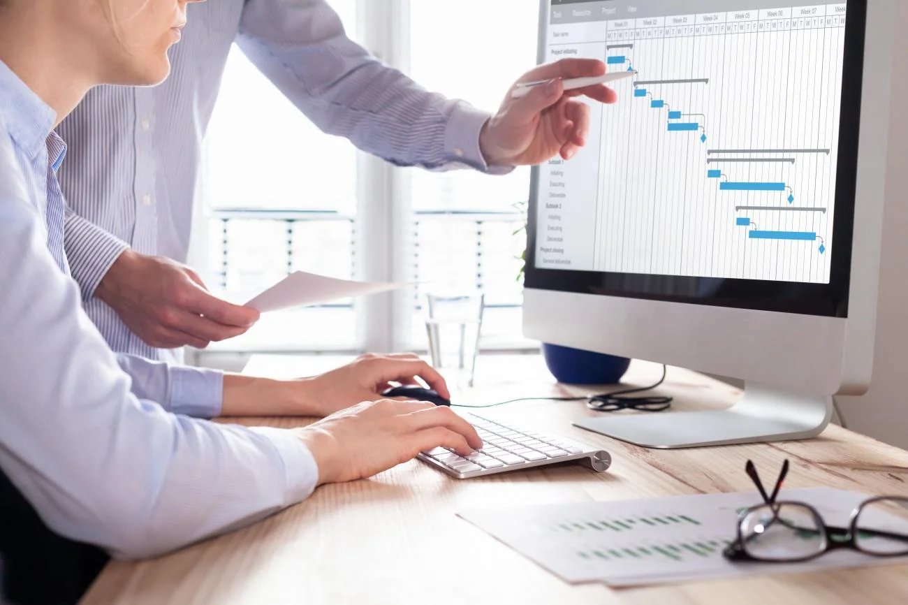Two people reviewing a project schedule on a desktop computer
